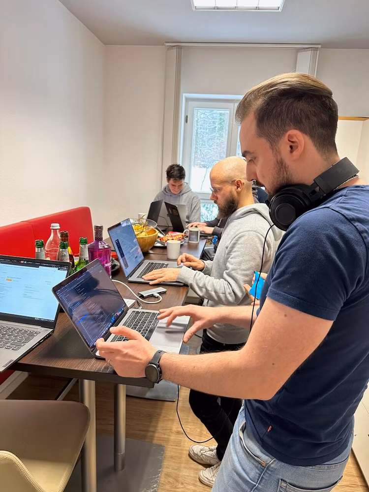Mehrere Personen stehen an einem Tisch und arbeiten am Laptop
